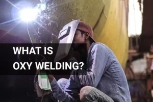 A skilled worker performs oxy welding techniques on a large ship hull in a bustling outdoor shipyard, showcasing the precision and safety of metal fabrication.