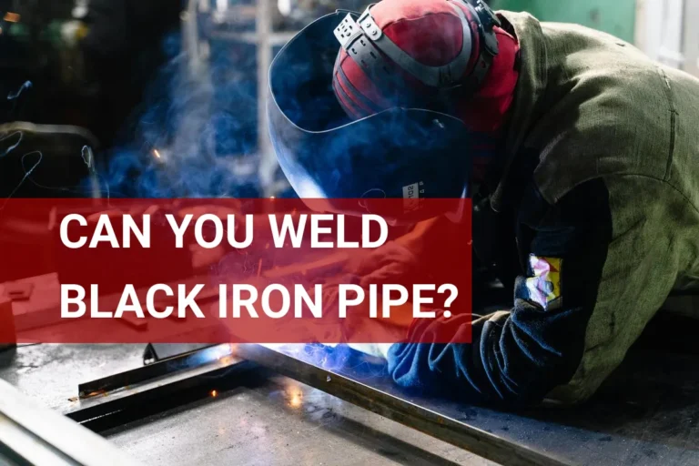 A skilled welder fabricates black iron pipe indoors, producing bright sparks and smoke from the welding process.