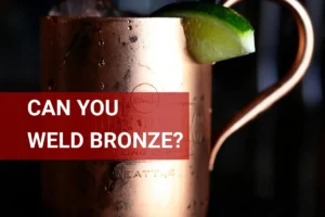 Close-up of a bronze cocktail mug, highlighting the welding craftsmanship, filled with a refreshing drink and garnished with a lime slice in a dimly lit setting.