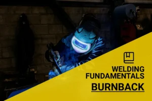 Welder in protective gear performing burnback welding in a workshop, with sparks flying.