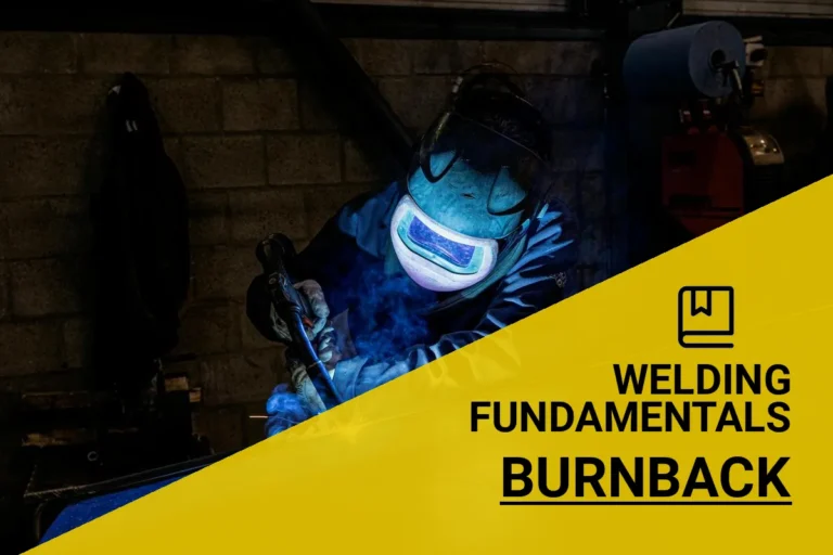 Welder in protective gear performing burnback welding in a workshop, with sparks flying.