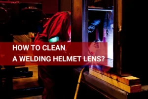 A welder in protective gear cleaning the lens of a welding helmet while surrounded by bright sparks and industrial equipment.