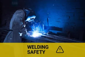Industrial worker welding zinc plated steel indoors, creating bright blue sparks and smoke.