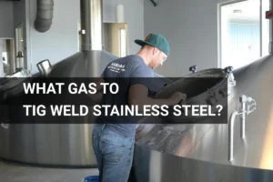 A worker tig welding stainless steel fermentation tanks using argon gas in a brewery.